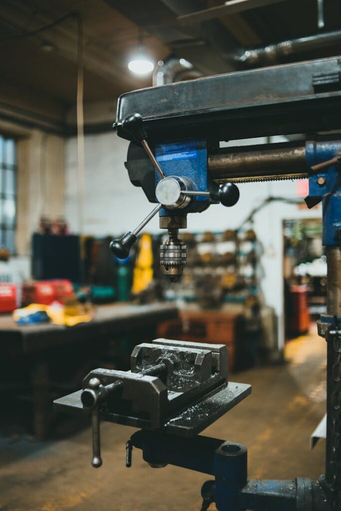 pexels-photo-9754811 Close-up of an industrial drill press in a workshop with various tools in the background.